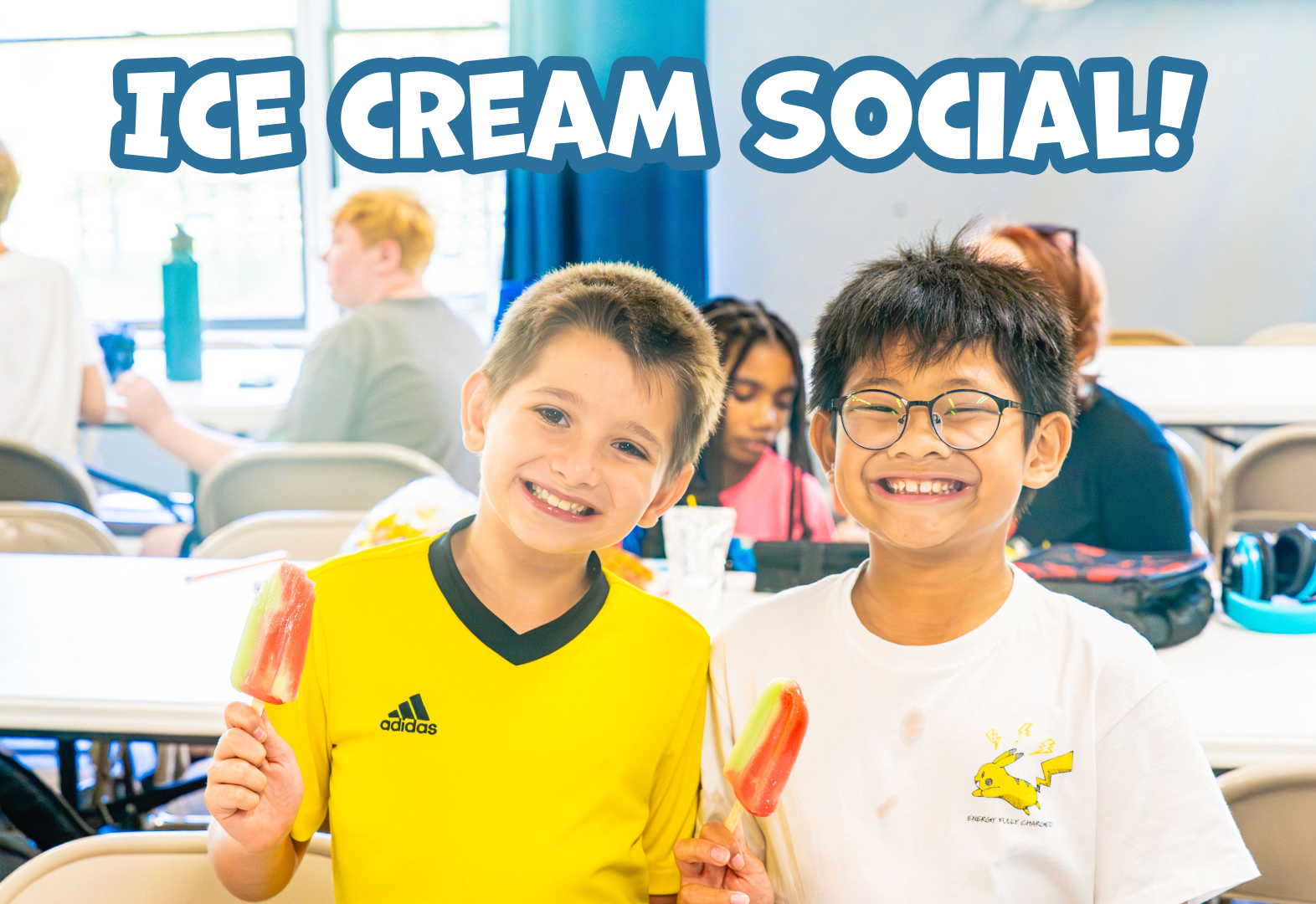 Two boys smiling and holding popsicles at an indoor ice cream social event.