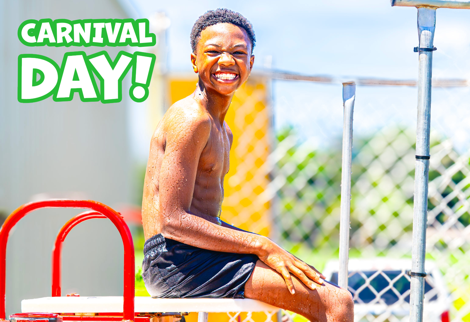 Boy in wet swim trunks sitting on diving board with carnival day text in background