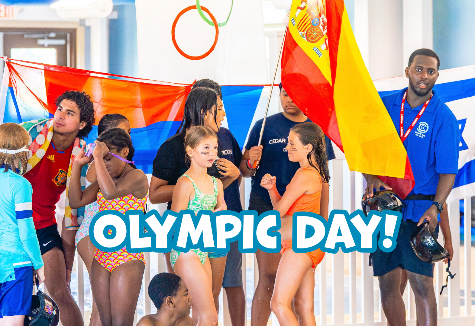 Children and adults indoors holding international flags with Olympic Day text displayed.
