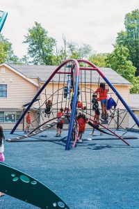 Children playing on a climbing structure with nets on blue rubberized flooring at a playground.