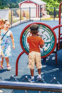 Children playing at a playground with a round maze panel and a blue rubber surface.