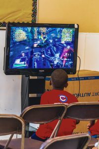 Child in red shirt playing a video game on a Philips TV indoors with cardboard boxes nearby.