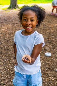 Young girl outdoors holding several earthworms in her hand and smiling at the camera