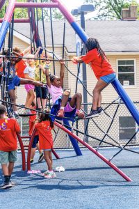 Children climbing and playing on a rope and metal bar structure at a playground with blue ground.