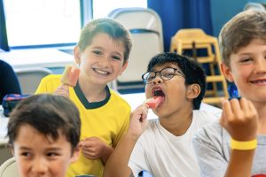 Four boys indoors eating popsicles, with two boys smiling and enjoying their treats.
