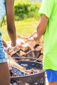 Two people roasting hot dogs over an outdoor fire pit with wood logs burning.