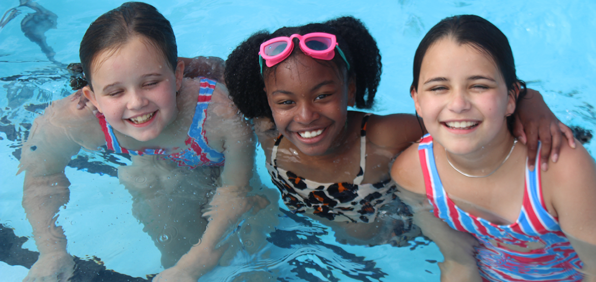 Three children in a pool smiling for the camera.