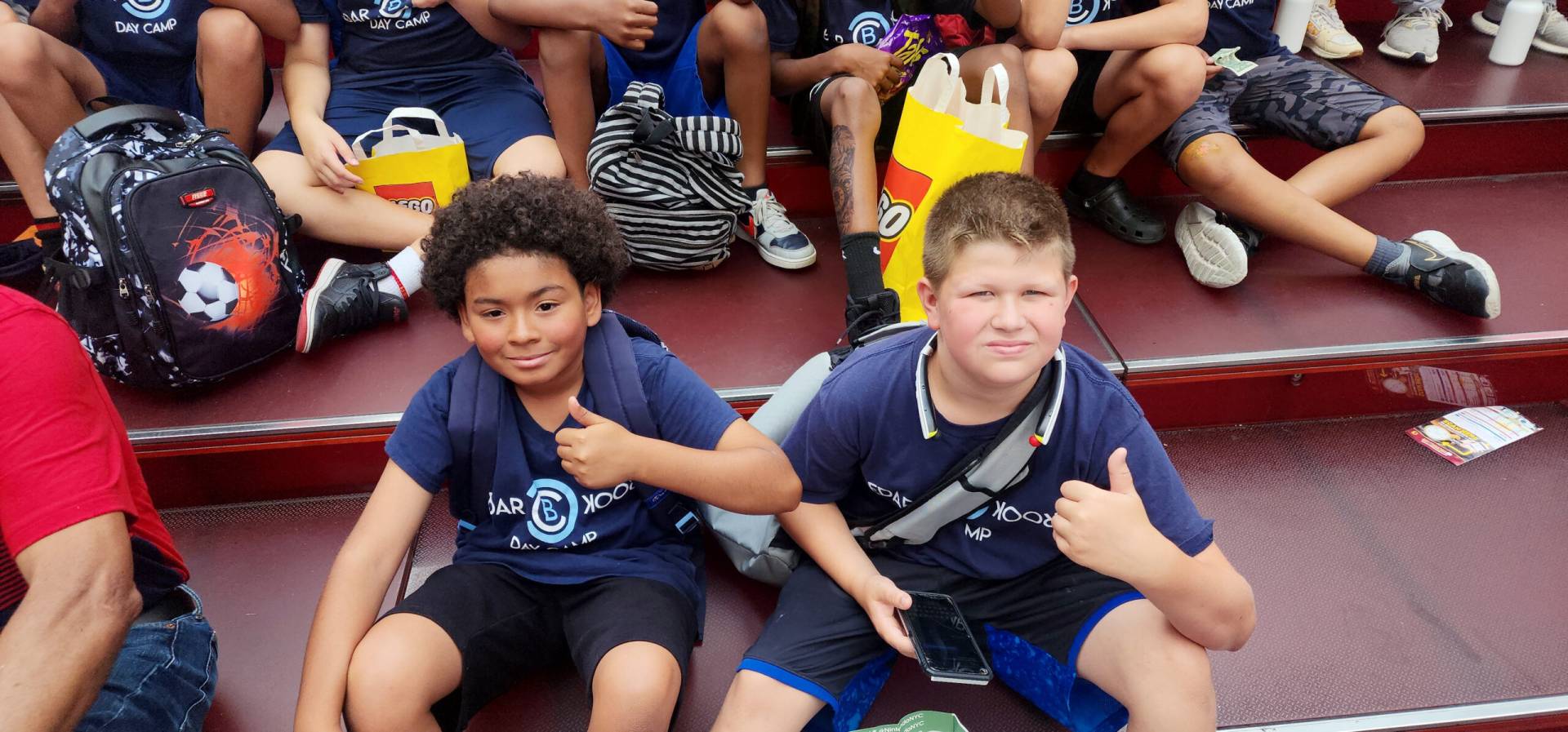 Two boys sitting on the ground with their thumbs up.